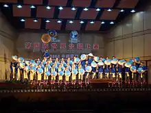 Chorale, en uniforme bleu et jaune, sur scène durant un concert.