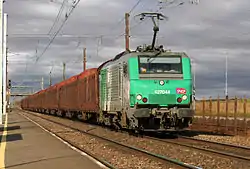 BB 27044 tirant des wagons de grumes vides passe en gare de Monnerville.