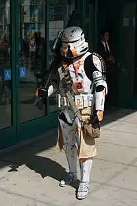 Homme portant une armure futuriste intégrale blanche, avec un casque décoré de orange.