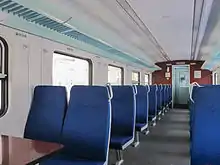 Photographie de l'intérieur d'un train : deux rangées de deux sièges bleus côte à côte.