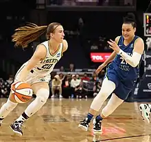 Une joueuse de basket-ball dribble avec sa main droite pour prendre de vitesse un défenseuse.