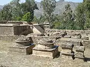 Dans les montagnes, le stupa principal en ruines, circulaire sur une plateforme carrée, entouré des plateformes des petits stupas.