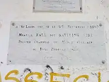 Est écrit en lettres capitales sur une plaque commémorative placée sur un mur : « A St Louis, est né le 22 septembre 1897 Mbarick Fall dit Battling Siki premier champion du monde africain de boxe professionnelle - 1897 – 1925 »
