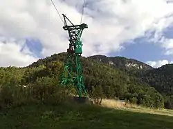 Pylône peint en vert, avec une petite plateforme et un matelas, et une montagne boisée en arrière-plan.