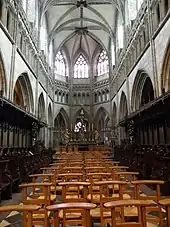 Photographie d'un choeur d'église avec le maître-autel, des stalles et le centre occupé par des chaises