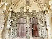 Photographie d'un intérieur de porche d'église, avec des parties en granite, d'autres en calcaire et des statues d'apôtres