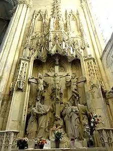 Grand groupe sculpté représentant trois hommes sur des croix. À leurs pieds, 7 personnages pleurant. Tout autour de cette scène, baldaquin sculpté.