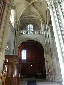 Chapelle avec une peinture murale rouge, surmontée par une tribune ouverte sur le collatéral nord. À droite, l'une des entrées de la basilique est visible.