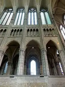 Trois piliers sont visibles reliés par un mur de pierre. Au-dessus, le triforium  et quatre fenêtres hautes de verre blanc.