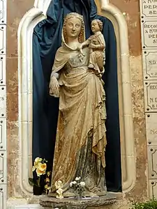 Dans une niche, statue en pierre, peinte par endroits, d'une femme tenant un enfant avec son bras gauche. L'enfant présente la tête d'un adulte. Aux pieds de la statue, deux vases contenant des fleurs ainsi qu'une statue d'angelot sont présents.