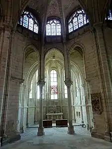 Chapelle contenant du mobilier en bois et un groupe sculpté accroché au mur de droite, surmontée de trois vitraux décoratifs.
