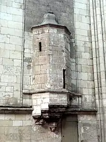 Echauguette en encorbellement avec un toit de pierre ressemblant à une cloche. En bas à droite, une vieille porte en bois