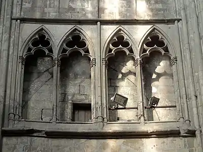 Entre un arc brisé et deux fenêtres vitrées, une galerie ouverte par des arcades composées de 5 lancettes séparées par des colonnettes