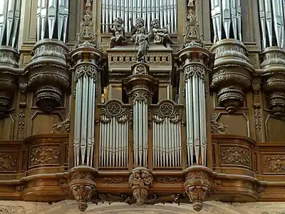 Parties inférieures d'un grand buffet d'orgue en bois, avec trois statues d'angelots musiciens et une statuette d'homme chevelu au centre de l'image.