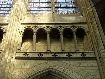 Entre un arc brisé et deux fenêtres vitrées, une galerie ouverte par des arcades composées de 5 lancettes séparées par des colonnettes