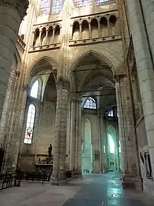 Grande arcade de pierre donnant accès au déambulatoire. Des tirants de bois soutiennent les voûtes. A gauche de l'arcade, un autel est aménagé et supporte une statue en bois.