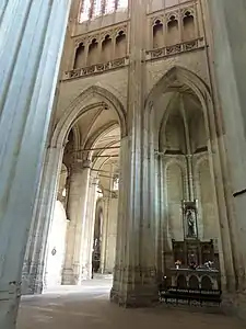 Grande arcade de pierre donnant accès au déambulatoire. Des tirants de bois soutiennent les voûtes. A droite de l'arcade, un autel est aménagé et supporte une statue en bois.