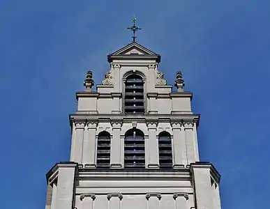 Parties supérieures de la tour avec une croix surmontée d'un coq dorée et, un peu plus bas, deux têtes sculptées de saint Quentin avec les clous sur chaque épaule.
