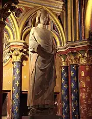 Statue de pierre peinte au milieu d'un décor gothique.