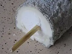 Vue en coupe d'un fromage cylindrique d'où dépasse une paille.