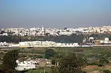 Vue sur les hauteurs de Salé (quartier Bettana) depuis Rabat, terrains vagues et palmiers au premier planc