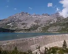 Un barrage retenant un lac avec en arrière plan une parois rocheuse.