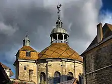 photographie en couleurs du haut de deux tours, l'une carrée, l'autre ronde, recouvertes de tuiles et se terminant chacune par un clocheton.