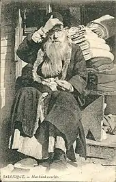 photographie noir et blanc : un homme barbu devant des rouleaux de tissu.l« Marchant israélite » de Salonique, av. 1918.