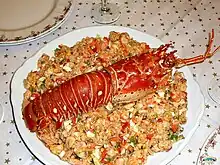 Une langouste entière cuite posée sur des fruits de mer et des légumes en fins morceaux.