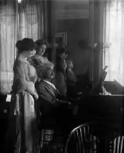Photographie de Mark Twain jouant du piano, avec sa fille, debout et une amie derrière lui