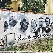 Photographie d'un mur avec des portraits de personnages peints ; un coffret en bas à gauche et un texte sur le bas et sur toute la longueur.