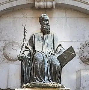 Image d'une statue représentant sous une arche un homme barbu assis tenant dans sa main droite un rameau et dans sa main gauche une plaque gravée.