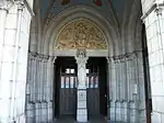 Le porche et l'entrée. Sur le pilier centrale est placée une statue de Notre-Dame de Lourdes. Sur le tympan du portail sont représentés le Christ pantocrator et le tétramorphe