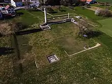 Vue depuis le dessus d'un champ avec plusieurs murs en ruines et deux colonnes blanches.