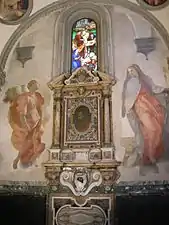 Fresque. L'ange et Marie se dressent de part et d'autre d'un monument commémoratif comprenant le portrait d'un homme.