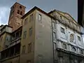 photo : le coin d'un bâtiment et sa haute façade. Au fond la tour carrée du clocher.