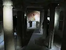 Photographie en couleurs d'une pièce sombre dont le plafond est supporté par des colonnes.