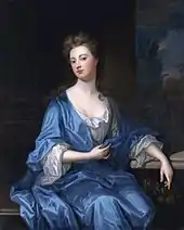 Portrait en pied d'une femme assise portant une robe bleue.