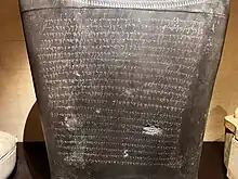 Three quarter view of a large black stone inscribed with 22 lines of Phoenician text.