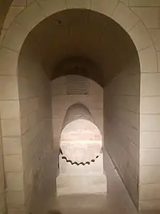Fût de colonne en pierre réemployé en sarcophage, dans une niche de pierre.