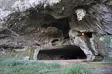 Vue de l’entrée d’une grotte, s’ouvrant comme une bouche dans une falaise de calcaire gris clair.
