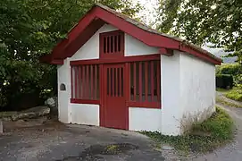 Vue d’un petit oratoire, maisonnette aux murs blancs et aux boiseries rouge sang.