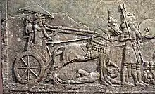 Le roi Sargon II, sur un char écrasant un ennemi, regardant l'assaut d'une cité ennemie.