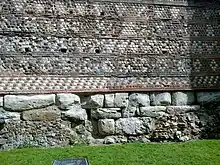 Fragment d'un mur avec une base comportant plusieurs niveaux de grosses pierres et d'autres niveaux avec des petites pierres et des briques, formant un décor géométrique