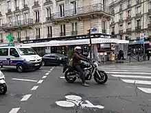 Un deux-roues motorisé arrêté après la ligne d'effet du feu tricolore, sur un sas vélo.