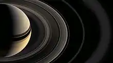 Une moitié du système saturnien est montrée, Saturne étant coupée en deux et montrant les arcs réalisés par les anneaux jusqu'aux plus externes.