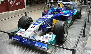 Photographie d'une monoplace de Formule 1 bleu foncé, blanche, vert clair, vue de trois-quarts, exposée.