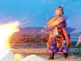 Photographie d'un homme couvert de fourrure dansant près d'un feu.