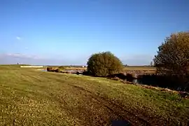 Photographie en couleurs d'un pré longé à droite par une voie d'eau