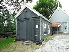 Photographie en couleurs d'un bâtiment en bois et d'une maison et de son appentis en arrière-plan